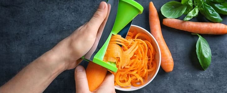 Woman using vegetable spiral slicer to make carrot spaghetti